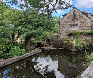 Rivière bordée d'une maison en pierre et d'arbres reflétés dans l'eau au Charmant mobil-home Pont-Aven