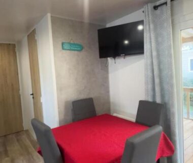 Intérieur avec table à nappe rouge chaises et télévision dans l'hébergement Chez Gill & Clo