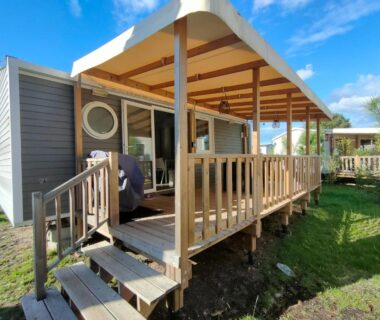 Terrasse couverte en bois avec escaliers et pelouse du bungalow Chez Seb et Sarah – Bungalow Paisible aux Viviers