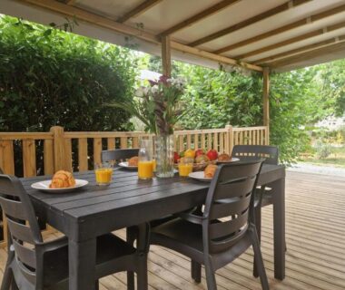 Terrasse couverte avec table dressée et jus d'orange au camping Clim, piscine, animations, concerts, jeux enfant