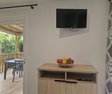 Coin séjour avec terrasse en bois télévision et bol de fruits au camping Clim, piscine, animations, concerts, jeux enfant