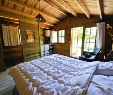 Chambre en bois avec lit double et baie vitrée donnant sur jardin dans le Gite le Verger