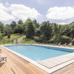Piscine extérieure entourée d'herbe et transats sur terrasse en bois au Domaine de Guillaume