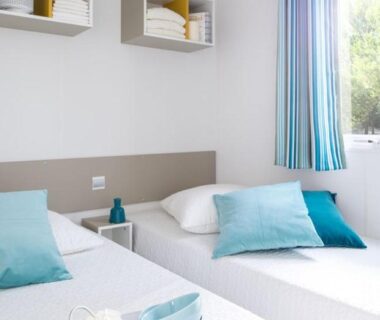 Chambre claire avec deux lits simples et coussins turquoise au Domaine de l'Epinette
