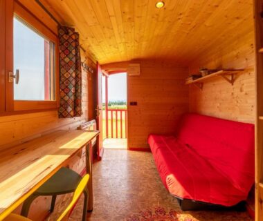 Intérieur de chalet en bois avec canapé rouge et bureau au Domaine de la Cambre