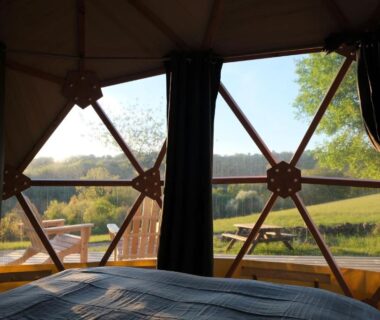 Intérieur avec lit et fenêtre panoramique sur prairie au Domaine de la Faurie