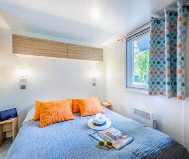 Chambre avec lit double coussins orange et fenêtre au Domaine de la Forge
