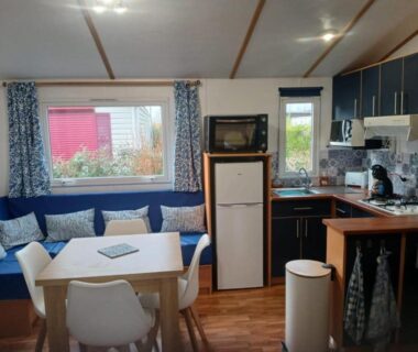 Intérieur de mobil-home avec salon, coin cuisine et table au camping Escapade aux Peupliers