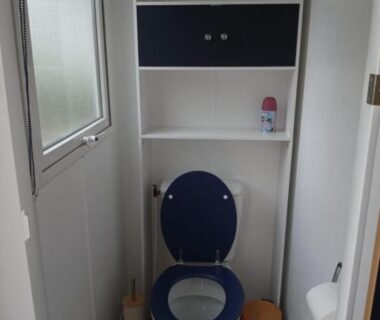 WC intérieur avec abattant bleu étagères et poubelle dans l'hébergement Escapade aux Peupliers