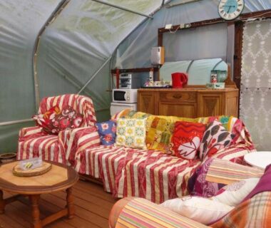 Salon couvert avec canapés colorés et coin cuisine dans le Fern Meadow Caravan