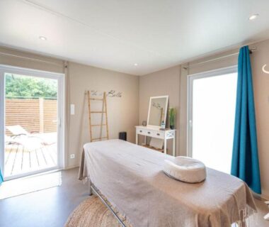 Salle de massage avec table de soin et portes vitrées au Flower Camping Au Bois des Biches