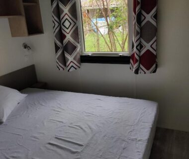 Chambre avec lit et fenêtre sur pelouse au camping Frédéric et Maëva