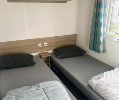 Chambre avec deux lits simples et fenêtre avec rideaux dans le GRS Mobil Home