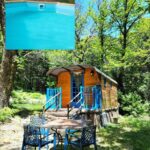 Roulotte en bois et espace repas sous les arbres avec piscine au Gite la bleuet