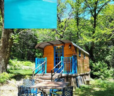 Roulotte en bois et espace repas sous les arbres avec piscine au Gite la bleuet