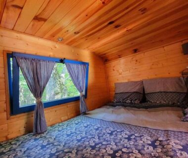 Chambre en bois avec lit double et fenêtre à rideaux bleus dans le Gite la bleuet