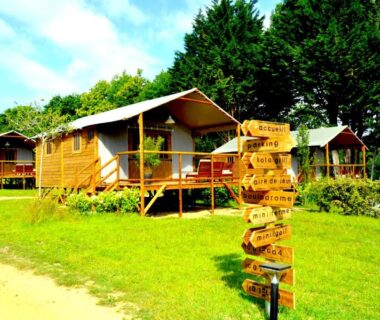 Prairie avec tentes sur pilotis et panneau directionnel au Glamping Terre & Mer