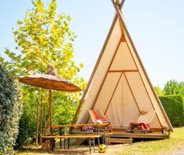 Terrasse en bois avec parasol et chaises devant tente tipi au Glamping Urrugne