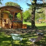 Emplacement herbeux avec roulotte en bois et chaises dans Graines de nature – Ecolodges Insolites