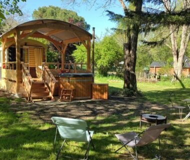 Emplacement herbeux avec roulotte en bois et chaises dans Graines de nature – Ecolodges Insolites