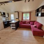 Intérieur séjour avec canapé d'angle rouge et kitchenette dans le Grand Mobile home dans camping