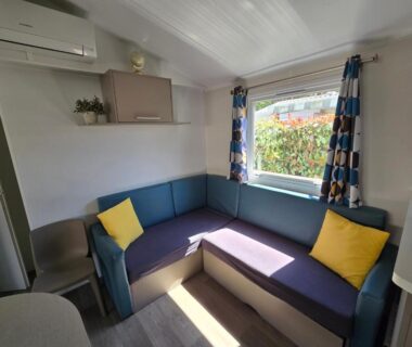 Intérieur coin salon avec banquette coussins et fenêtre dans Grands mobil-homes 4 chambres clim-parking privées-possibilité d’accueil jusqu’à 20 voyageurs Siblu