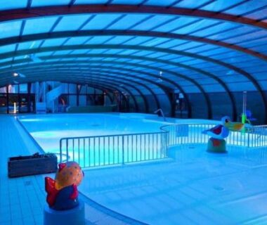 Piscine couverte intérieure bleue avec pataugeoire et dôme au Hebergement dans un Domaine à Litteau