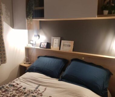 Chambre double avec tête de lit étagères et lampes dans le camping HerGine