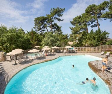 Piscine extérieure avec sol en bois et parasols au camping Huttopia Arcachon