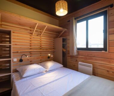 Chambre en bois avec lit double et fenêtre au camping Huttopia Arcachon