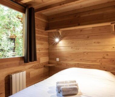 Chambre en bois avec lit et serviettes au Huttopia Dieulefit
