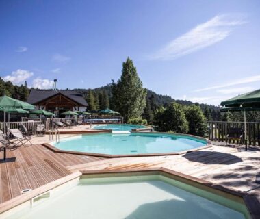 Terrasse en bois avec bassins, chaises longues et parasols sur fond de montagnes au Huttopia Font Romeu