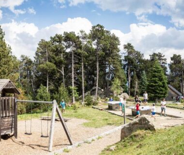 Aire de jeux en forêt avec balançoires et structure de jeux au camping Huttopia Font Romeu