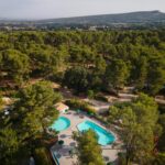 Piscine entourée de pins vue du ciel au camping Huttopia Fontvieille