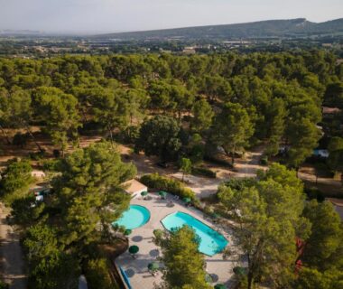 Piscine entourée de pins vue du ciel au camping Huttopia Fontvieille