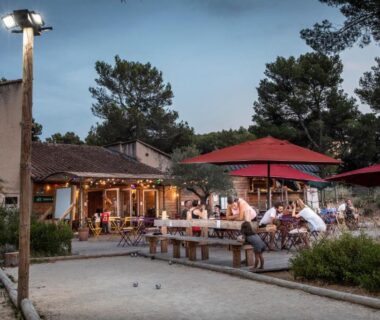Terrasse extérieure avec parasols rouges et convives au Huttopia Fontvieille