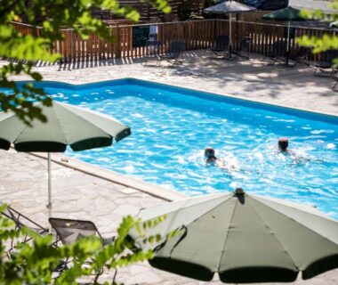 Piscine extérieure avec parasols et baigneurs au camping Huttopia Gorges du Tarn