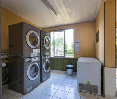 Buanderie avec lave-linge empilés et congélateur dans le camping Huttopia La Plage Blanche