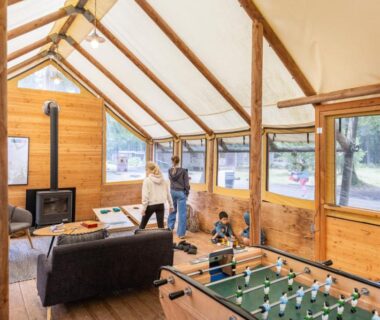 Salle commune en bois avec baby-foot et canapé dans le Huttopia Lac de Sillé