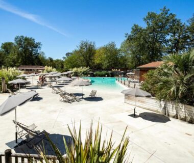 Solarium et piscine extérieure entourés d'arbres au camping Huttopia Lac de l'Uby