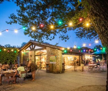 Terrasse extérieure avec tables et guirlandes lumineuses au Huttopia Le Moulin