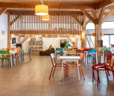 Salle commune avec tables en bois et comptoir au camping Huttopia Les Châteaux