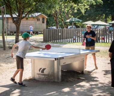 Aire de loisirs ombragée avec table de ping pong et enfants jouant au camping Huttopia Les Châteaux