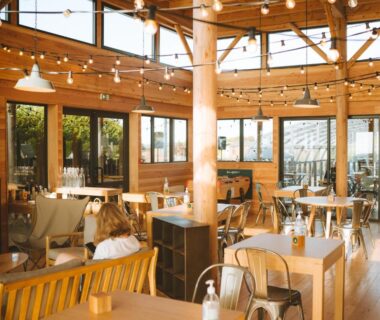 Salle de restaurant avec tables et guirlandes lumineuses au camping Huttopia Les Falaises – Normandie
