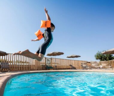 Bord de piscine avec une personne qui saute dans l'eau au camping Huttopia Meursault