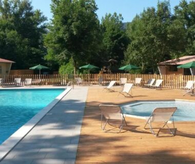 Piscine, pataugeoire et chaises longues sur solarium en bois au camping Huttopia Millau