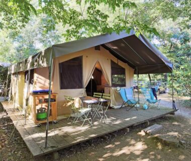 Tente lodge sur terrasse ombragée avec chaises et table dans le camping Huttopia Pays des Bastides