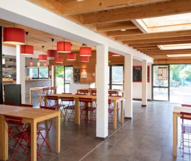 Salle commune avec tables et suspensions rouges au Huttopia Royat