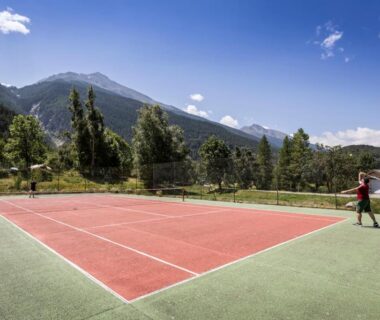 Court de tennis en plein air entouré de montagnes au Huttopia Val Cenis