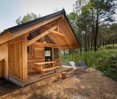 Chalet en bois avec terrasse et chaises dans les sapins au Huttopia Val Cenis